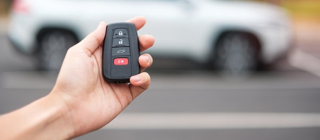 Рука держит смарт-ключ дистанционного управления автомобилем для блокировки или разблокировки дверей белого автомобиля Концепция безопасности путешествий и транспорта