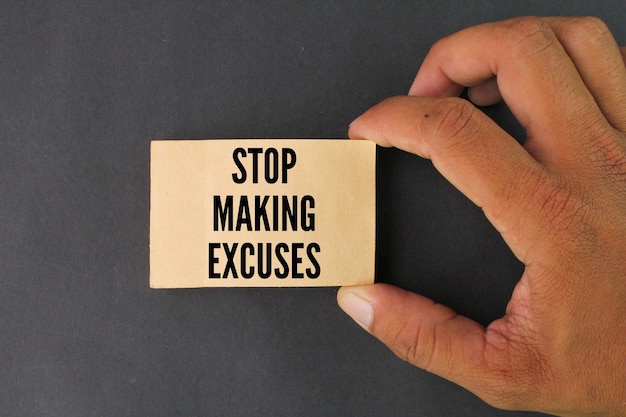 A hand holding a card that says stop making excuses.