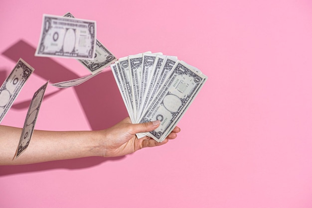 Hand holding cash on a pink wall