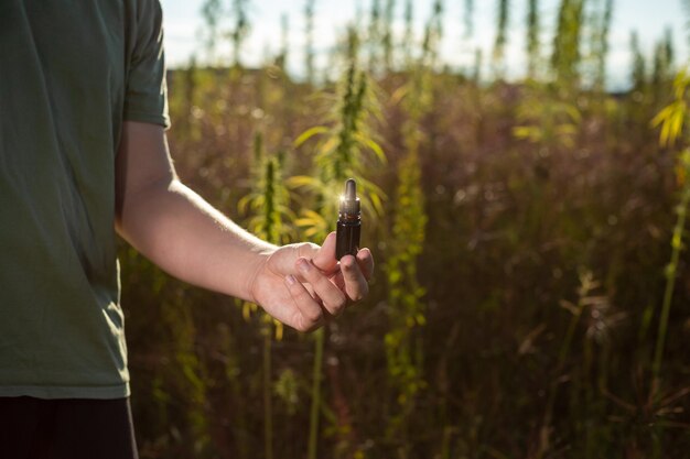 Hand holding a cbd dropper bottle between hemp plants