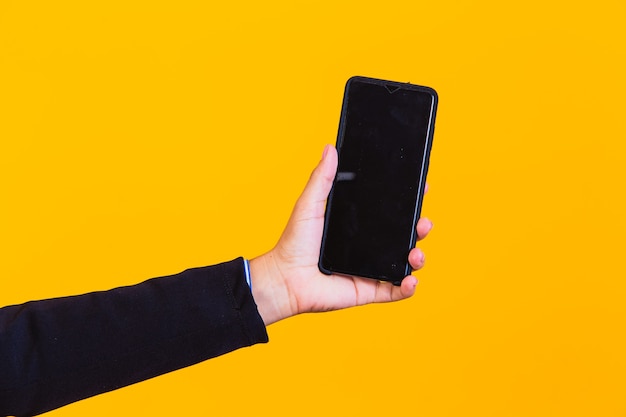 Hand holding a cell phone on yellow background with space for text.