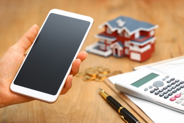 hand holding a  cellphone in front of house model