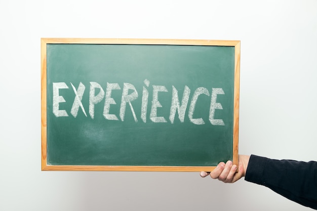 Hand holding a chalkboard with the word EXPERIENCE handwritten in chalk