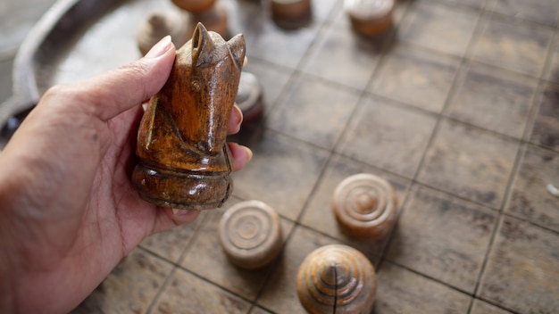 Foto mano che tiene il cavallo degli scacchi in legno lo sfondo è una scacchiera.