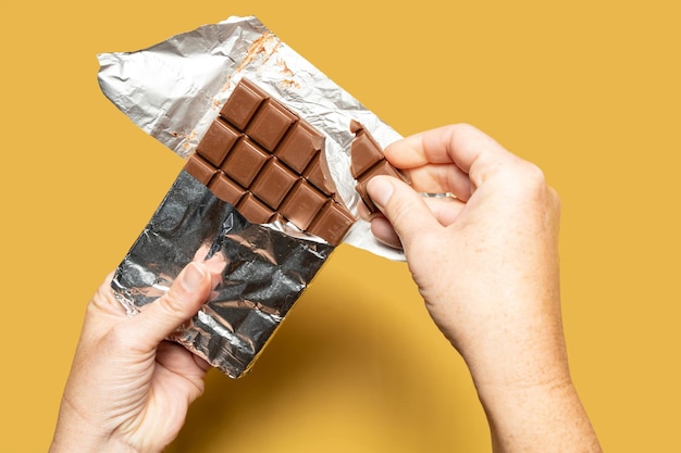 A hand holding a chocolate bar that is being held up by a hand.