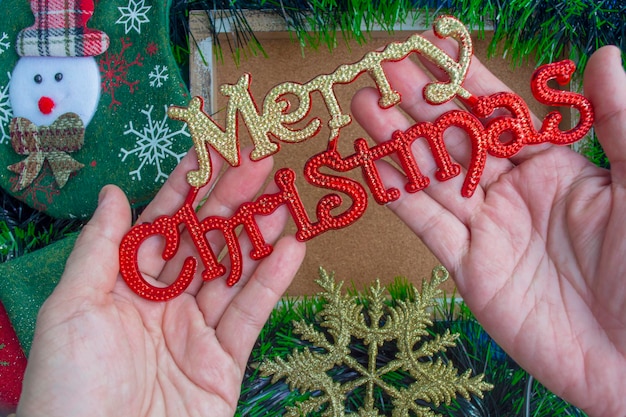 Hand holding Christmas decoration with background of fir tree and ornaments decor. Top view