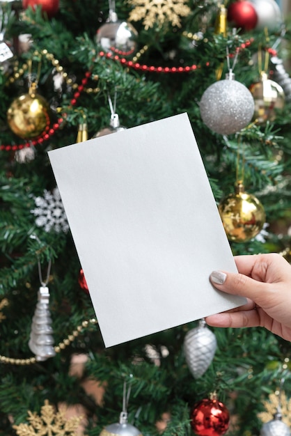 Carta del modello di progettazione di saluto di festa di natale della tenuta della mano sul fondo dell'albero di natale.