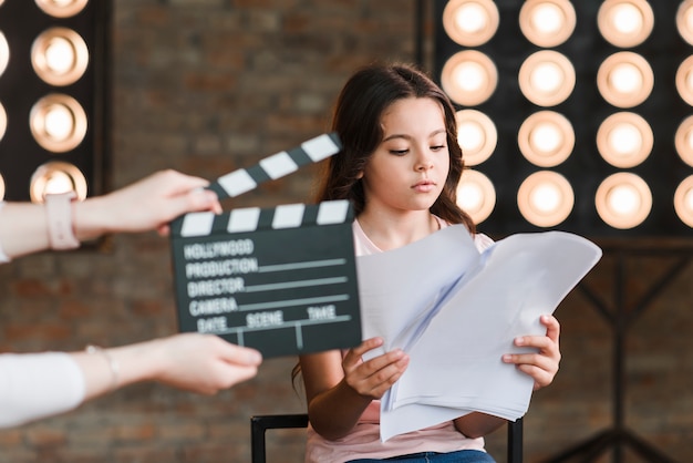 Photo hand holding clapper board in front of girl reading scripts in studio