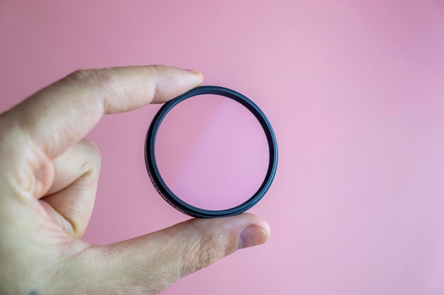 Hand holding clear camera filter, isolated on pink