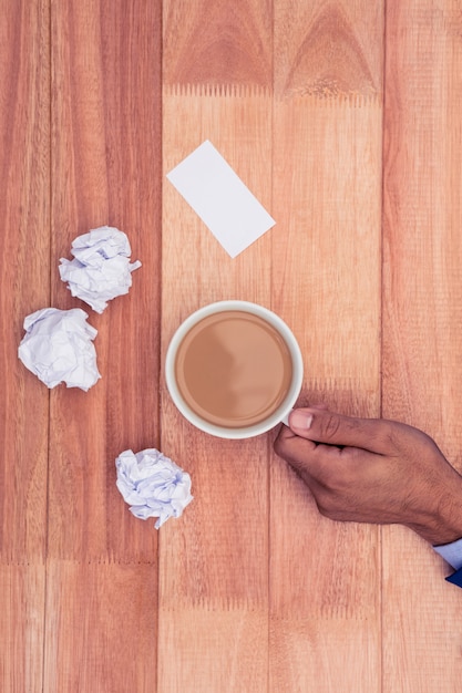 Hand holding coffee cup by paper balls on desk in office 