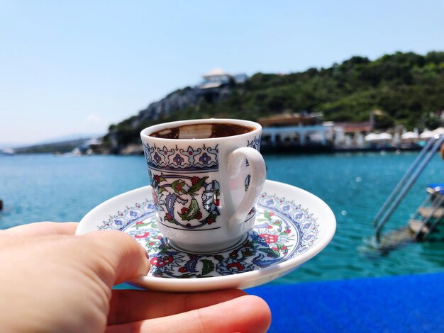Foto la mano che tiene la tazza di caffè vicino all'acqua
