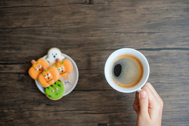 Hand holding coffee cup during eating funny halloween cookies\
happy halloween day trick or threat hello october fall autumn\
traditional party and holiday concept