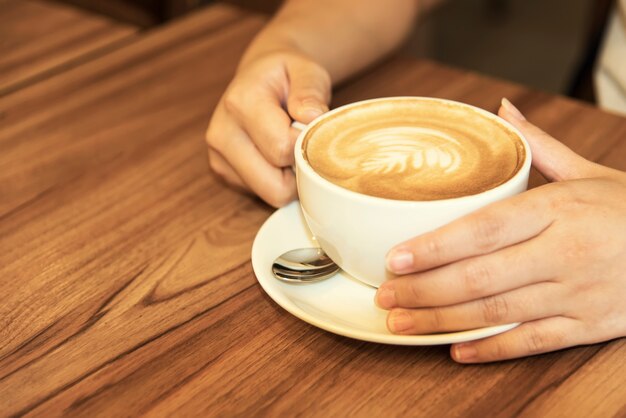 Hand holding coffee cup on wood table.