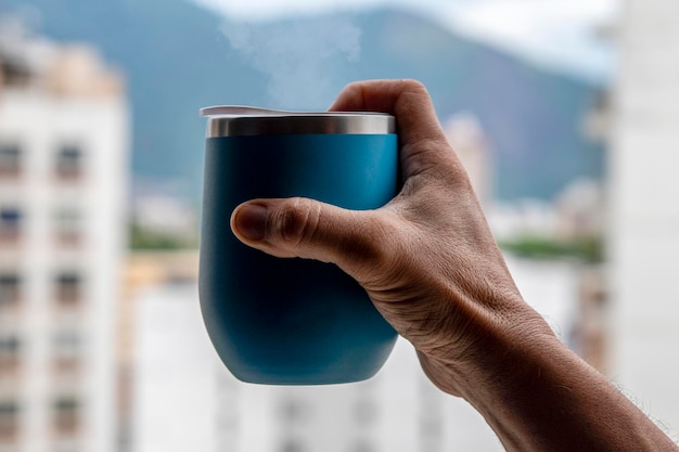 Hand holding a coffee mug coming out of smoke with urban environment background