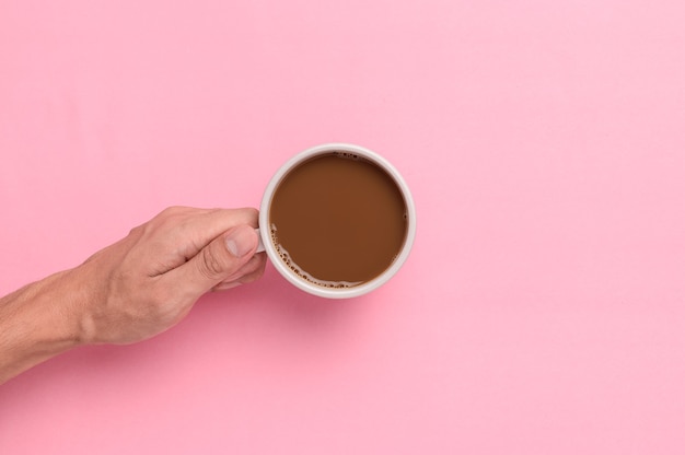 Hand holding a coffee mug on a pink background