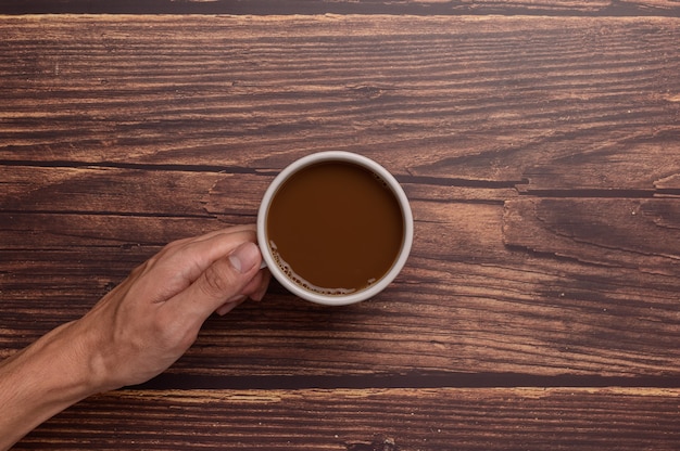 Mano che tiene una tazza da caffè su uno sfondo di legno