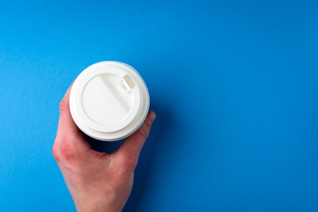 Photo hand holding coffee paper cup on blue background.