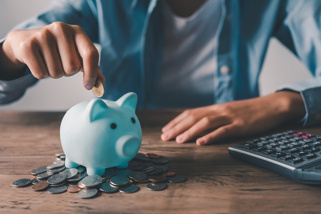 豚の貯金箱でコインを持っている手。貯蓄と金融口座の概念
