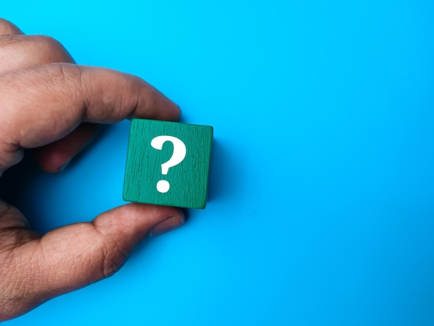 Hand holding colored cube with question mark symbol on a blue background with copy space