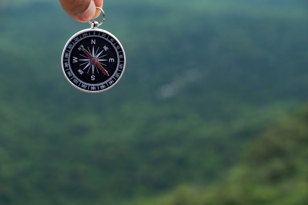 Hand holding compass against green tree montain background. 