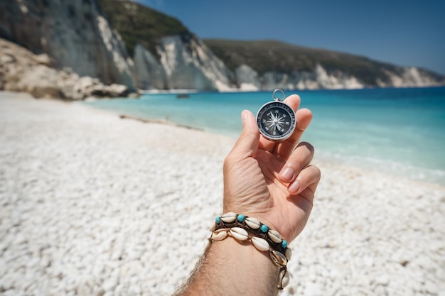 Hand holding a compass on the beach in background