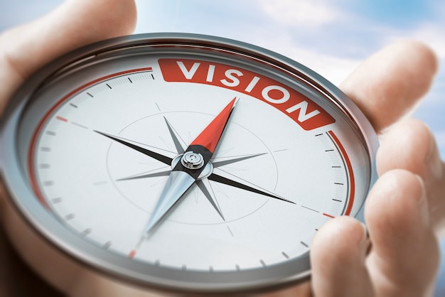 Photo hand holding a compass with needle pointing the word vision. company or organization statement values. composite image between a hand photography and a 3d background.