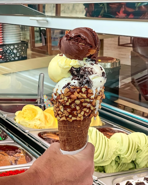 A hand holding a cone of ice cream with nuts on it.