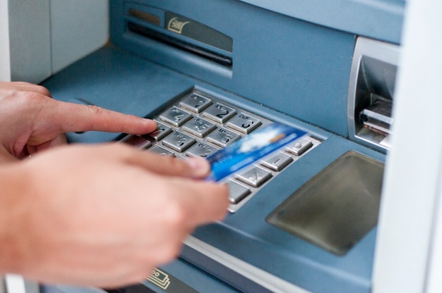 Hand holding a credit card next to an atm