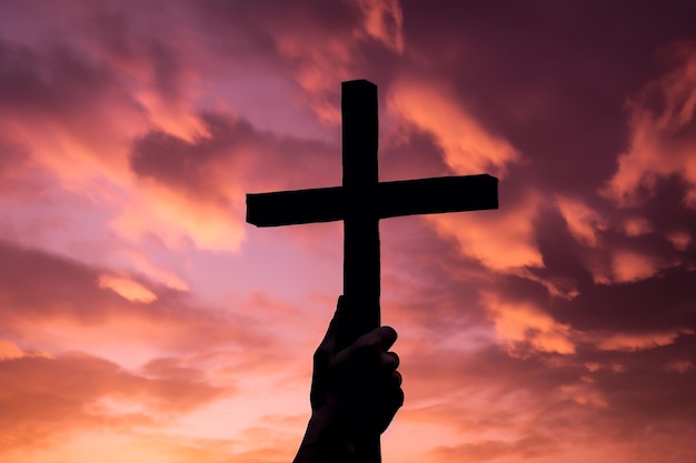 A hand holding a cross against a sunset sky