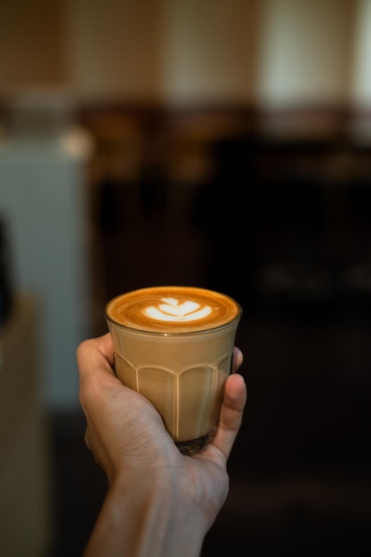 A hand holding a cup of coffee with latte art on it