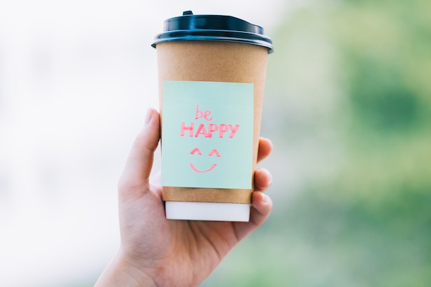「beHAPPY」という言葉が入った一杯のコーヒーを持っている手