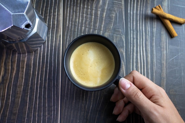 Hand holding cup of coffee over wooden table Top view