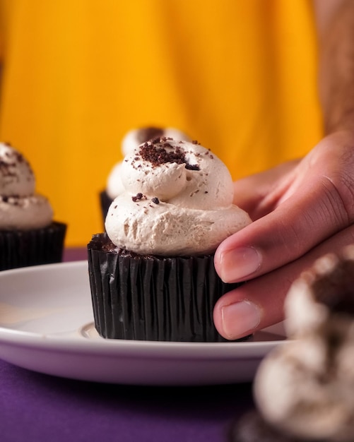 Foto mano che tiene un cupcake al cioccolato fondente su sfondo giallo