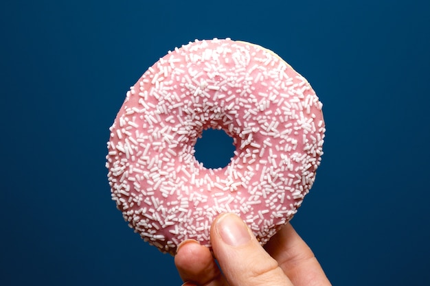 Hand holding a delicious colorful pink donut with sprinkles, sugar concept