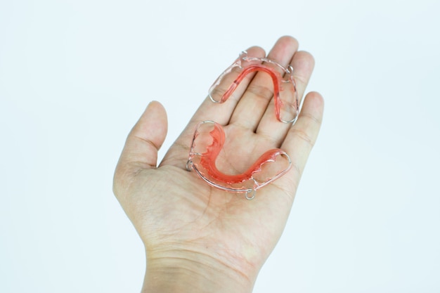 Hand holding dental retainer on white background.