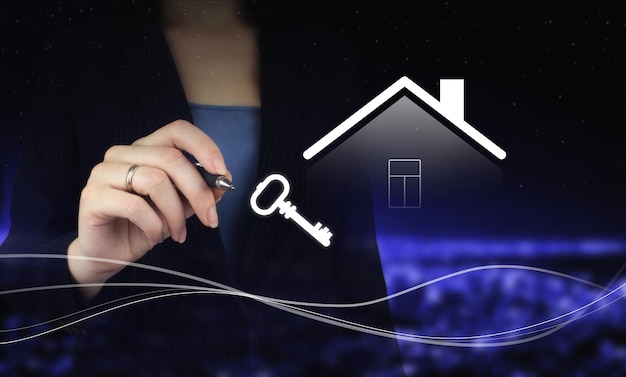 Hand holding digital graphic pen and drawing digital hologram Smart Home and Key sign on city dark blurred background. Real estate agent offer house, property insurance and security.