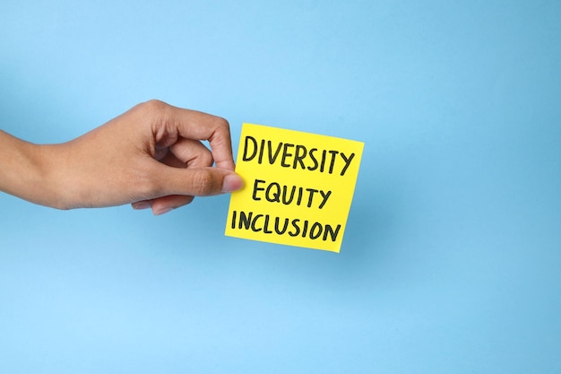 Photo hand holding diversity equity and inclusion text on yellow paper over blue background
