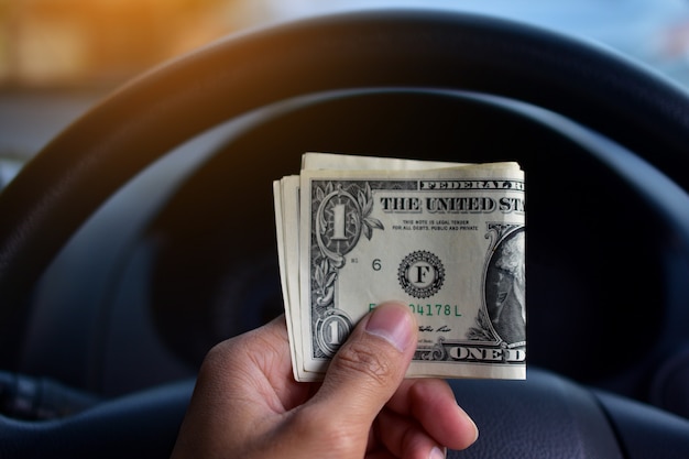 Hand holding dollar money in car