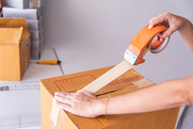 Hand holding duct tape to pack products to prepare shipments.