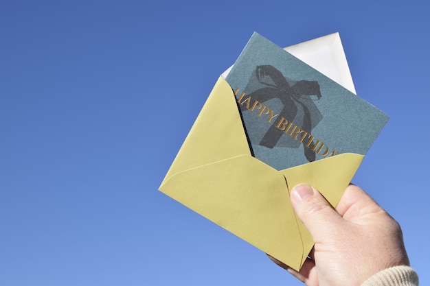 A hand holding an envelope that says happy birthday on it.