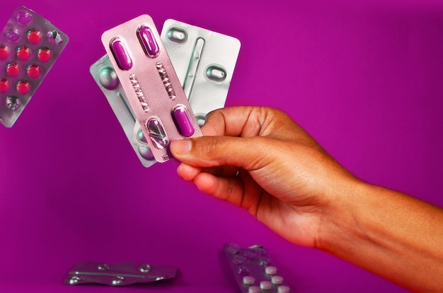 Hand holding on fingertips medicine pack with purple pills and other medicine packs on blurred backg