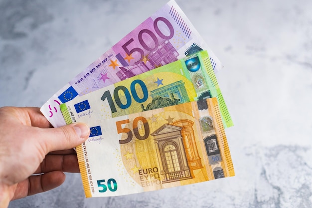 Рука держит пять и сто пятьдесят банкнот евро Деньги в руках мужчины на сером фоне