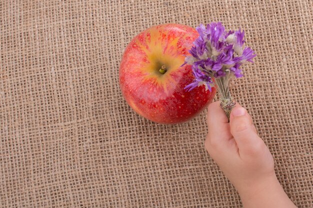 Hand holding flower bouquet beside an apple