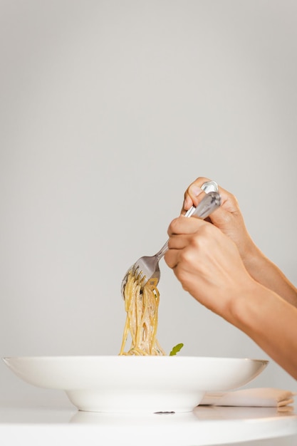 Mano che tiene la forchetta e il cucchiaio che mangiano la salsa di crema di tartufo di spaghetti