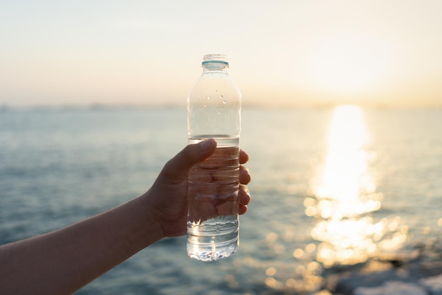 生活のための最高の健康のための海の背景の概念天然水でsutで新鮮な飲料水のボトルを持っている手