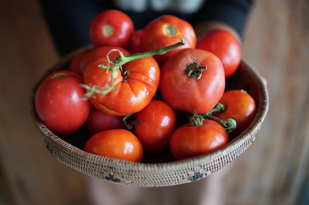 Hand holding fresh raw red tomatoes in wicker basket