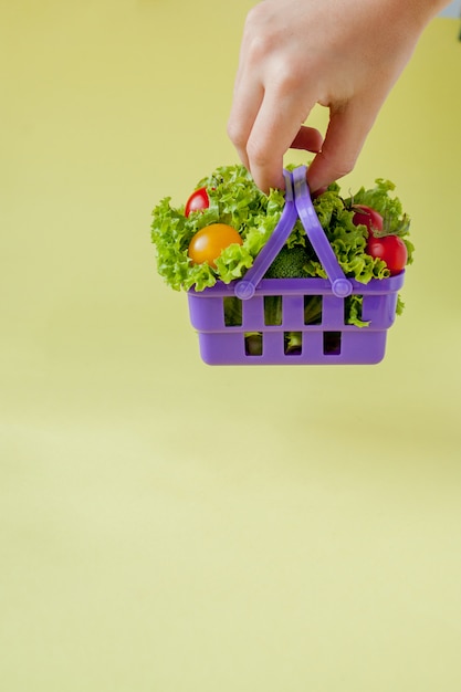 Hand holding fresh vegetables in basket on yellow background