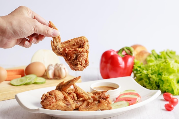 Hand holding fried chicken wings ready for eat on white table