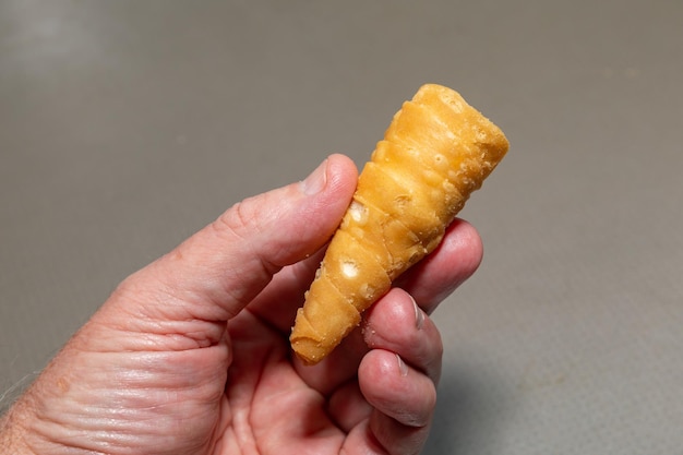 A hand holding a fried egg roll with a bite taken out of it.