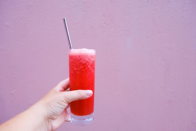 Hand holding a frosty watermelon drink with a metal straw against a pink backdrop